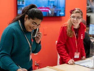 two teenage girls standing behind the till at a BHF shop and smiling as one of them speaks on the phone