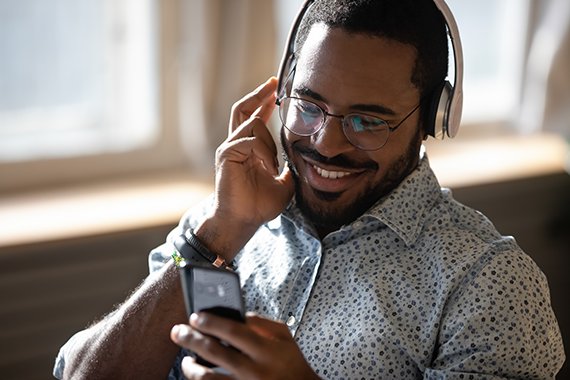 A person listening to something on their phone, wearing headphones and smiling.