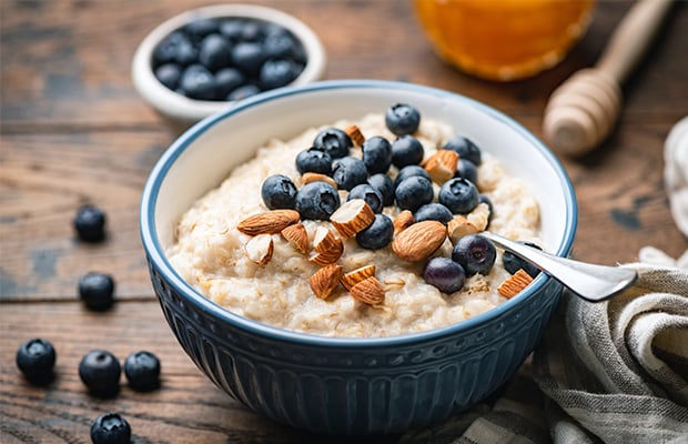 A bowl of porridge topped with blueberries and almonds on a table.