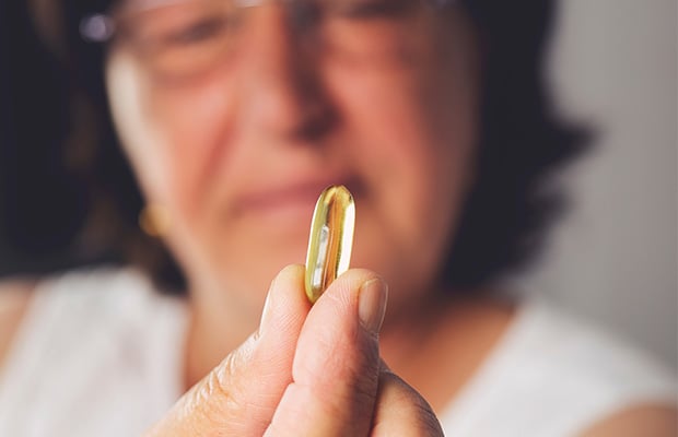 A woman holding a fish oil supplement capsule.
