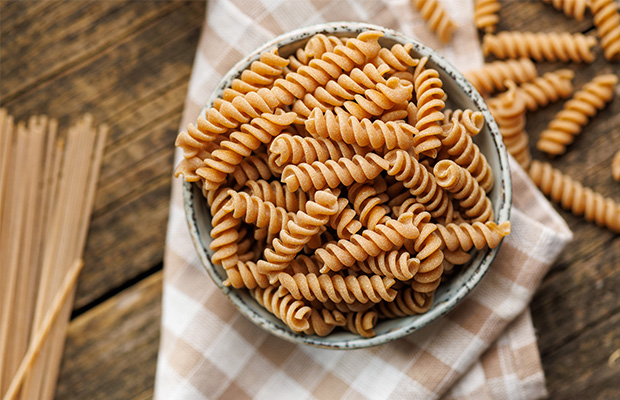 A bowl of uncooked wholegrain pasta on a table.