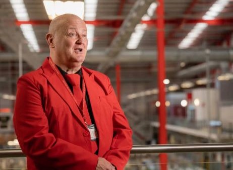 A men dressed in a red suit standing in a factory setting